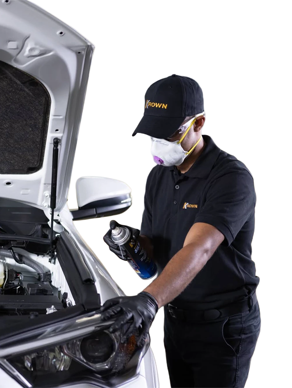 A Krown technician applying rust protection beneath an open hood