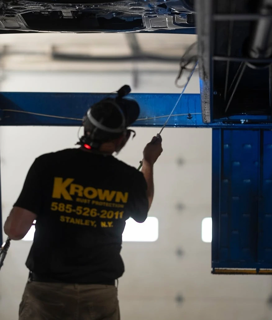 A Krown Stanley technician reaching the underside of a vehicle on the lift