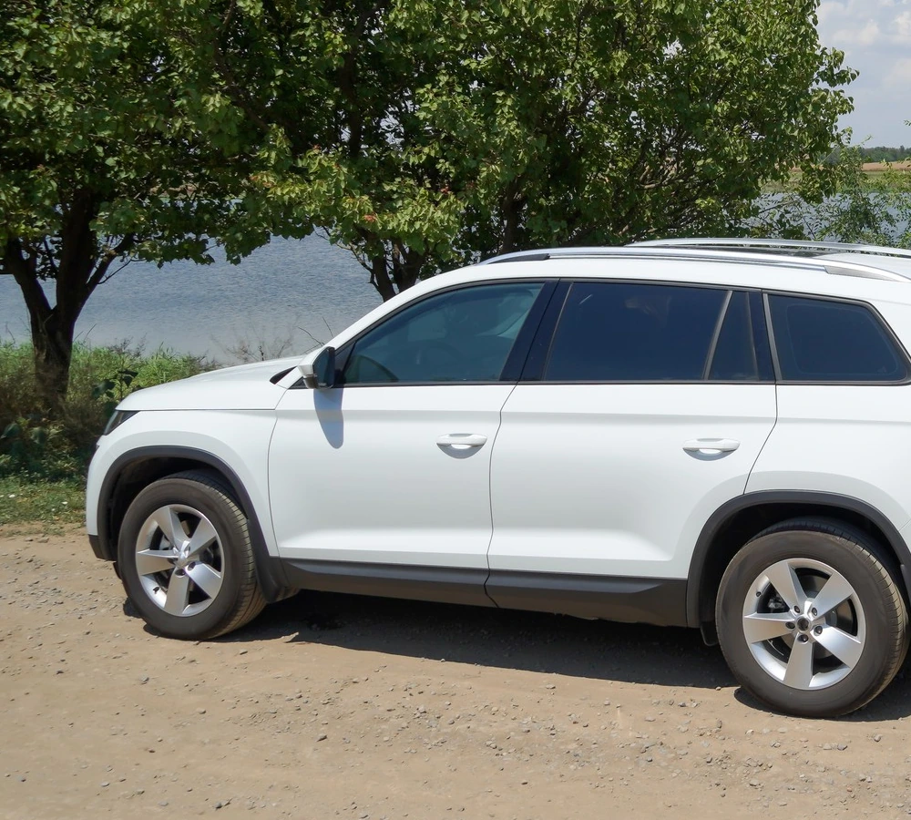 A white SUV parked on an unpaved surface beside a lake
