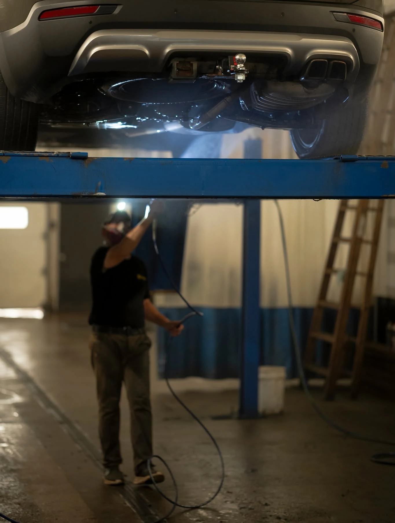 A technician spraying the underside of an SUV on the lift